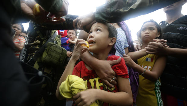 A Philippine air force officer hands out orange slices to typhoon survivors as they line up to board a C-130 military transport plane in Tacloban